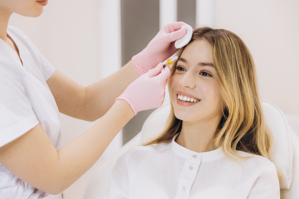 Cosmetician injecting botox into the forehead of a young, smiling woman in a modern beauty salon, enhancing her youthful appearance